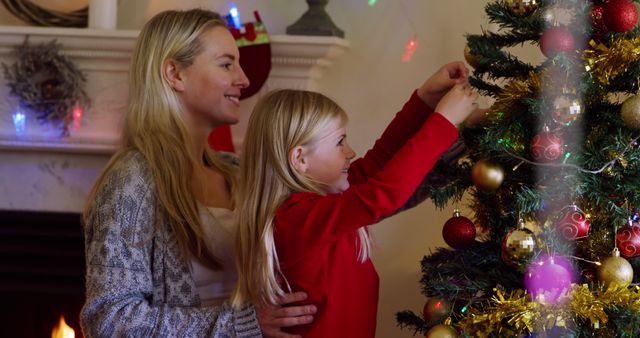Caucasian woman and girl decorate a Christmas tree at home. They share a festive moment, adding ornaments and enjoying the holiday spirit.