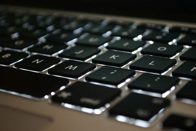 Close-up view of a backlit keyboard featuring black and silver keys, often used for illustrating themes on typing, computing, or technology. Great for tech blogs, articles related to office work or computing, and advertisements for technology products.