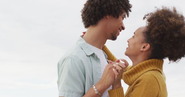 Young couple in affectionate embrace outdoors, enjoying a romantic moment. They look into each other’s eyes lovingly, sharing a candid smile. This image could be used in relationship advice content, lifestyle blogs, or promotional material for couple’s products.