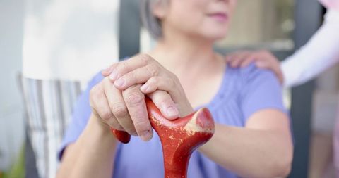 Senior asian woman gripping red cane while caregiver placing hand on shoulder outdoors