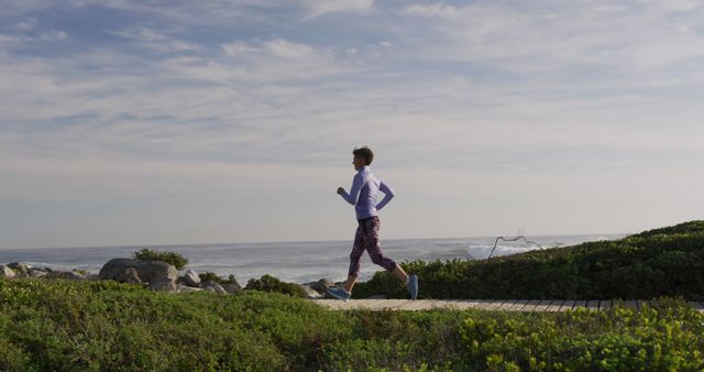 Woman jogs on a scenic coastal pathway with the ocean in the background. Ideal for illustrating topics related to outdoor fitness, healthy living, and leisure activities. Perfect for use in health blogs, fitness websites, tourism brochures, and exercise guides.