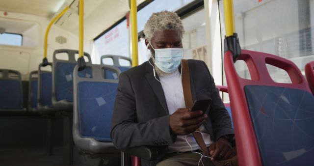 Middle-aged businessman wearing mask and using smartphone while commuting on public transportation. Can be used for articles on commuting during pandemics, public transportation safety, work-life balance, and mobile technology. Highlights safety measures during commute.