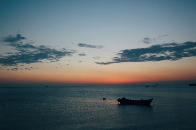 Calming image of a sunset with tranquil ocean waters and the silhouette of a boat in the foreground. Ideal for travel blog posts, relaxation apps, meditation screensavers, or inspirational quotes on social media.