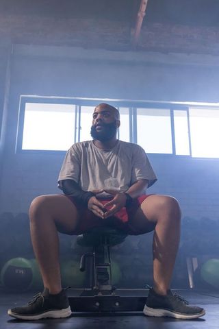 African american man sitting on bench resting after workout in moody industrial gym