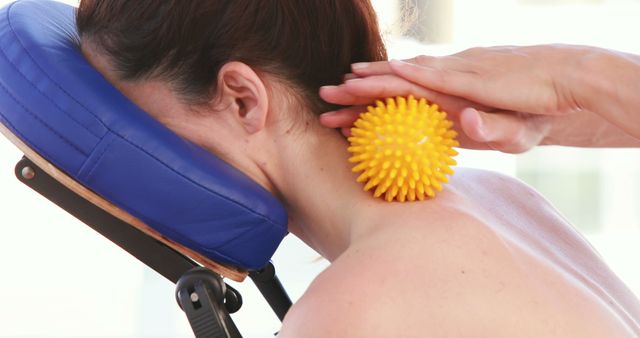 A Caucasian woman receives a massage therapy using a textured yellow ball, with copy space. Massage therapy is often used for relaxation and to alleviate muscle tension or pain.