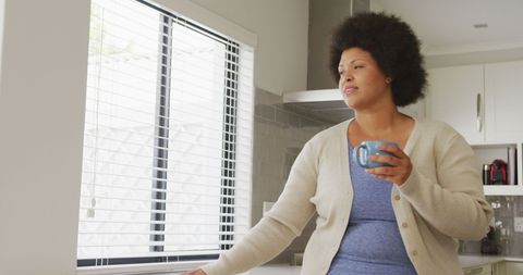 Woman Enjoying Coffee and Using Smartphone in Modern Kitchen