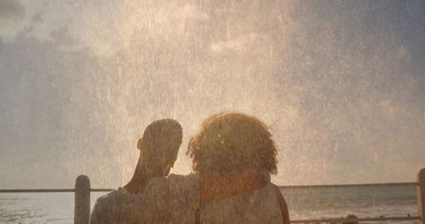 Sunlit ocean mist embracing couple at golden hour, backlit seaside silhouette