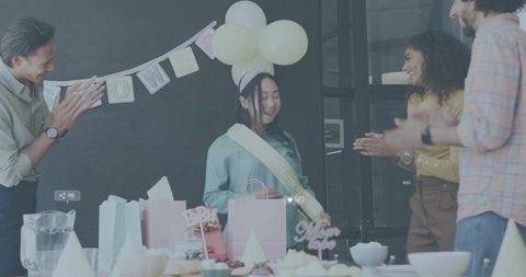 Smiling woman celebrating baby shower wearing sash and balloon headband at pastel party