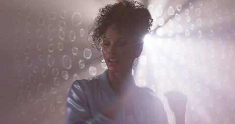 Backlit woman posing in satin bomber jacket with bokeh lensflare and dreamy pastel haze