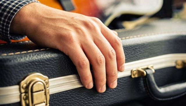 Right hand resting on black hardshell guitar case with brass latch closeup
