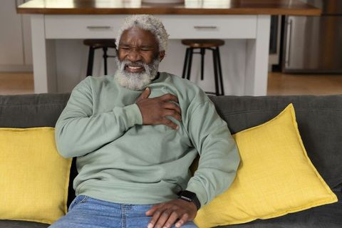 Senior african american man clutching chest on sofa experiencing chest pain at home