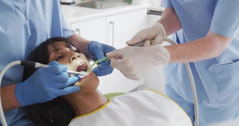 Dental team performing oral exam using suction and mirror on reclining patient