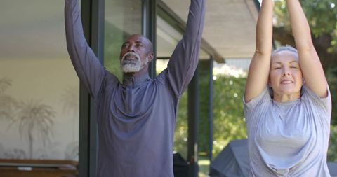 Mature couple stretching on sunlit patio performing gentle morning yoga and outdoor fitness
