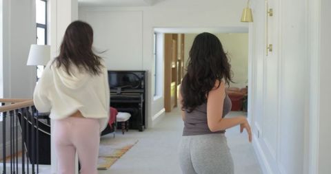 Diverse women wearing loungewear walking down bright modern hallway toward piano and open room