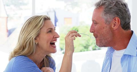 Smiling wife feeding husband for breakfast at home