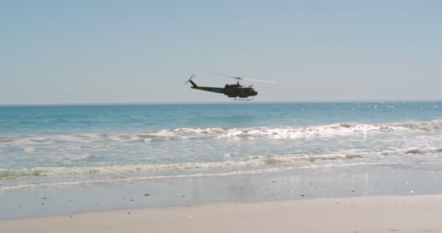 Helicopter flying over serene beach with calm ocean waves and clear sky. Ideal for aviation magazines, travel brochures, and defense-related articles.