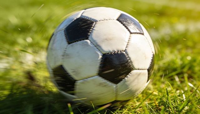 Sunlit soccer ball skidding across green grass, scuffed black-and-white panels in motion
