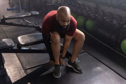 Athlete tying shoelaces on bench preparing workout in gym with dumbbells and medicine balls