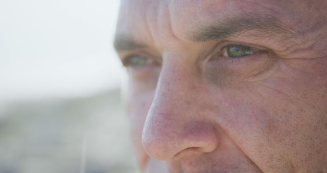 Close up of eyes thoughtful senior caucasian man on sunny beach looking away, copy space. Contemplation, retirement, wellbeing and active senior lifestyle, unaltered.