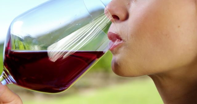A close-up captures an Asian woman drinking red wine directly from the glass, with copy space. Her lips are pursed, and the clear glass reveals the wine's rich color, suggesting a moment of casual enjoyment or tasting.