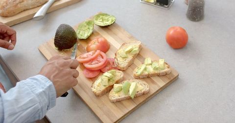 Man Preparing Fresh Avocado Toast on Wooden Board in Kitchen