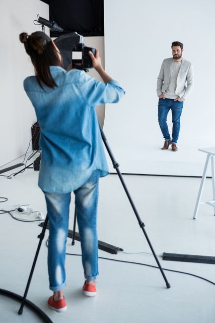 Male model posing for a photoshoot in a professional studio. Ideal for use in fashion magazines, photography tutorials, modeling portfolios, and advertisements for clothing brands. The image captures the behind-the-scenes process of a photoshoot, showcasing the interaction between the model and the photographer.