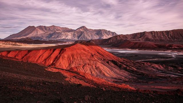 Crimson eroded butte glowing in low sunlight over salt playa and layered desert basin