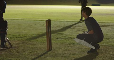 Floodlit night cricket wicketkeeper crouching at stumps watching batsman at crease