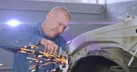 Mechanic grinding car frame for restoration in workshop