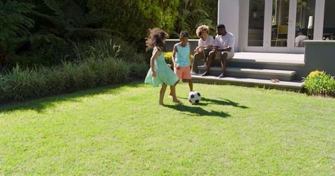 Family Enjoys Watching Children Play Soccer in Sunlit Backyard