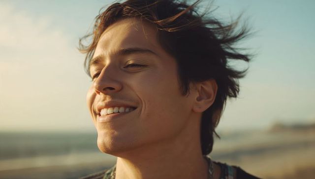 Smiling young man soaking up warm sea sun at beach during golden hour