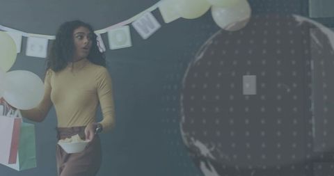 Woman holding balloon and gift bag turning during office celebration with pastel decor
