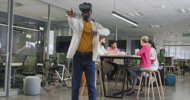 Happy african american businessman using vr headset over colleagues in office. working in business at a modern office.