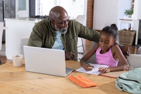 African american father helping daughter with homework at kitchen table using laptop