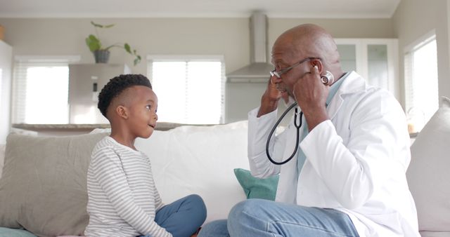 Doctor explaining stethoscope to young boy at home. Ideal for use in educational or healthcare-themed promotions, family health articles, or pediatric care brochures.