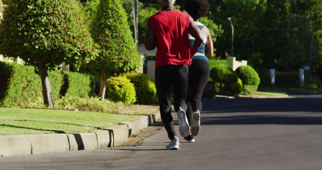 African american senior couple exercising outdoors running in sunny green road. healthy retirement and active lifestyle.