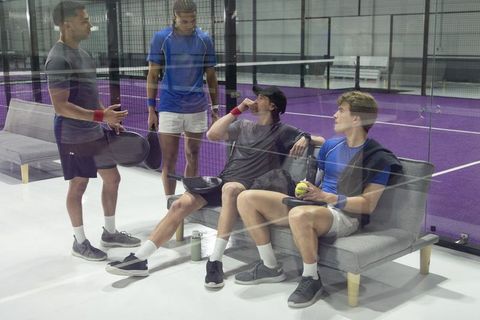 Padel players resting and chatting behind glass on indoor purple court