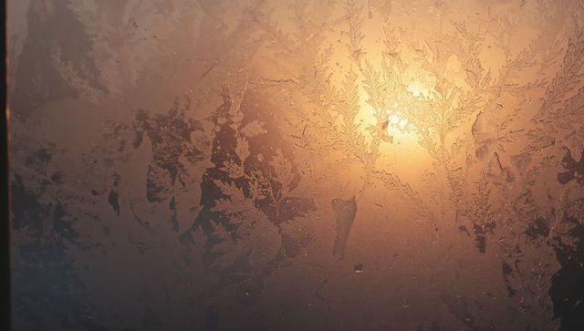 Amber sunrise glowing through frosted window glass with intricate ice fern patterns