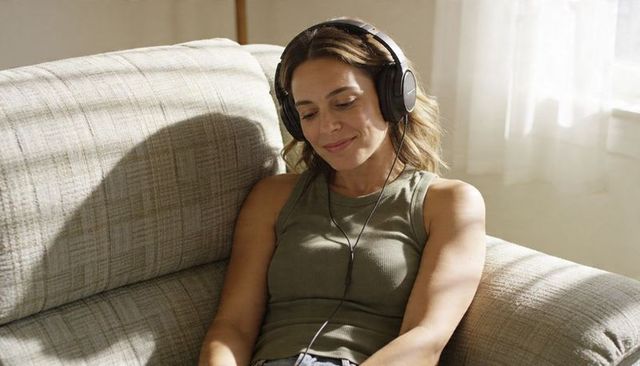 Sunlit woman listening to music with over-ear headphones on cozy beige sofa serene lifestyle