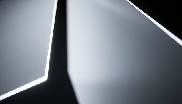 Minimalist edgelit geometric ceiling panels forming v junction with slate matte finish