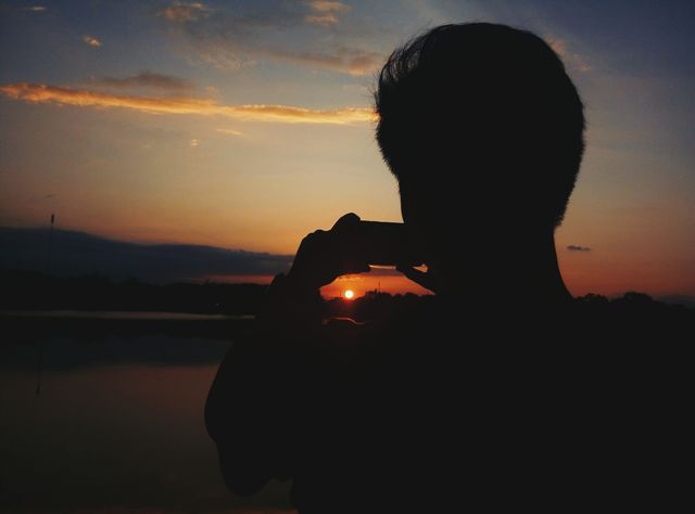 Person capturing photo of beautiful sunset by tranquil lake. Ideal for themes of nature, serenity, tranquil evenings, and moments of reflection. Can be used for travel, leisure, and photography articles or blog posts.