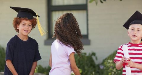 Children wearing graduation caps celebrating preschool diploma ceremony outdoors in sunshine