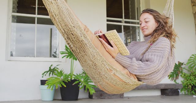Smiling caucasian woman lying in hammock reading book on terrace. healthy living, close to nature in off grid rural home.
