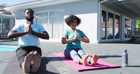 Diverse couple practicing yoga on poolside patio with mats and water bottle for wellness