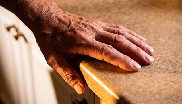 Resting senior male hand on warm kitchen countertop edge revealing veined wrinkled skin and brass pu