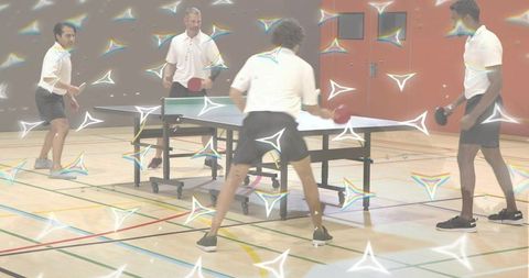 Four men playing doubles table tennis in gymnasium during energetic competitive rally