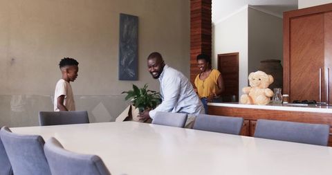 African American family carrying potted plant and smiling at dining table