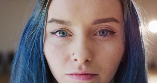 A close-up shot of a woman with blue hair and winged eyeliner, looking directly into the camera with a serious expression. This can be used in beauty blogs, makeup tutorials, fashion magazines, or advertisements focusing on cosmetics and hairstyling.