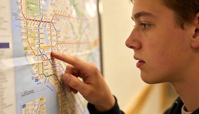 Teenager studying subway map and pointing route on wall map in hallway, planning commute