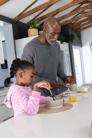 African american man teaching child breakfast prep at kitchen island in bright modern home